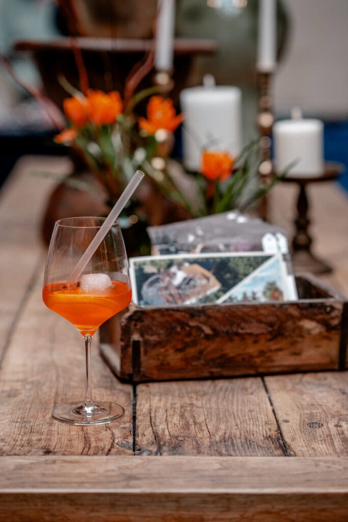Erfrischender Orangencocktail auf rustikaler Holztisch mit Blumen und Kerzen im Hintergrund.