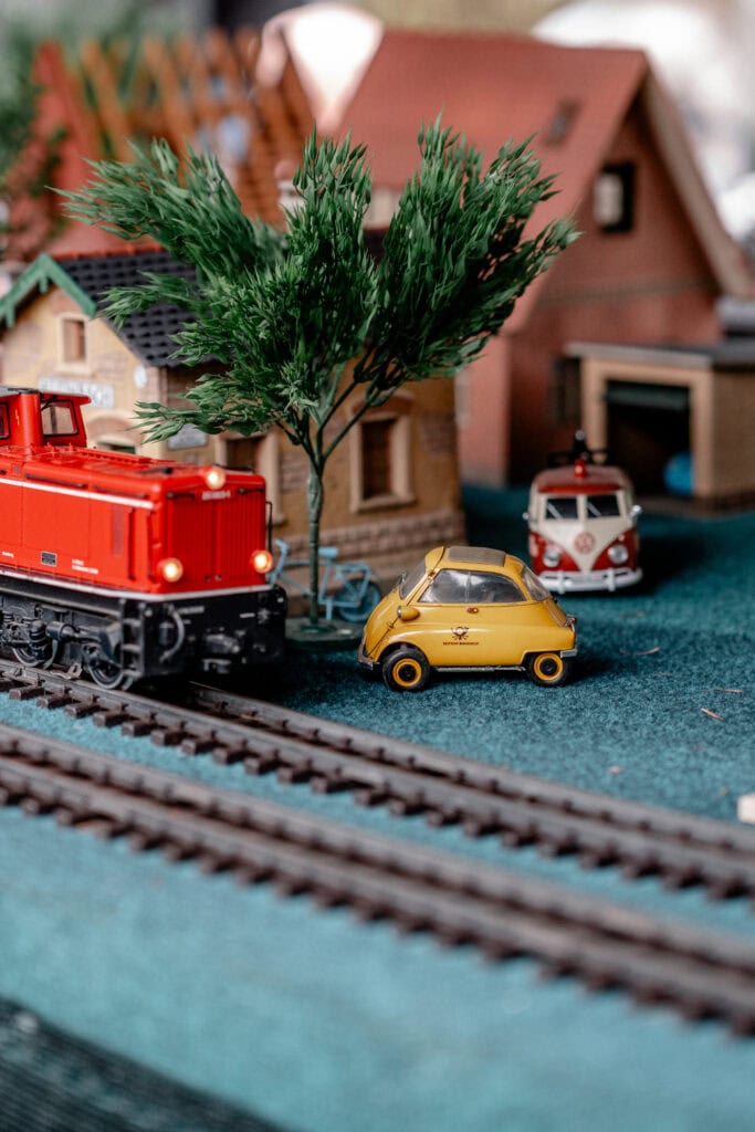 Spielzeugzug, Auto und Häuser auf Modellbahn mit Baum, für nachhaltiges Leben.