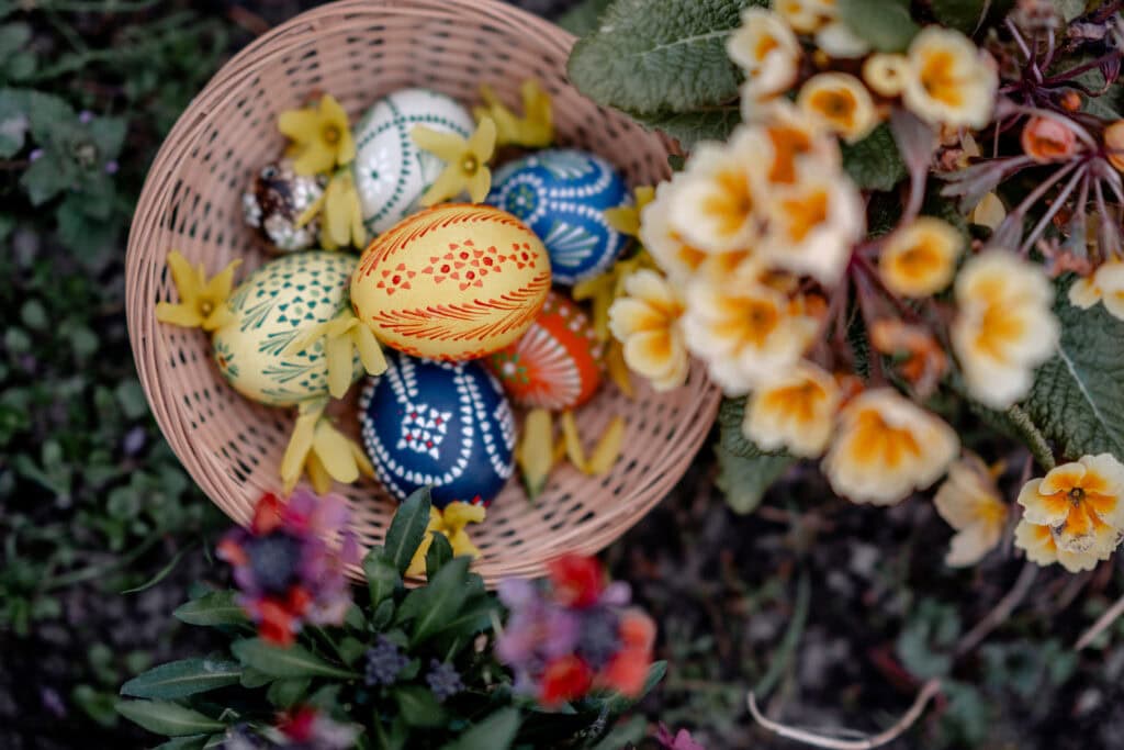 Osterkorb mit bunten, handbemalten Ostereiern und Frühlingsblumen.