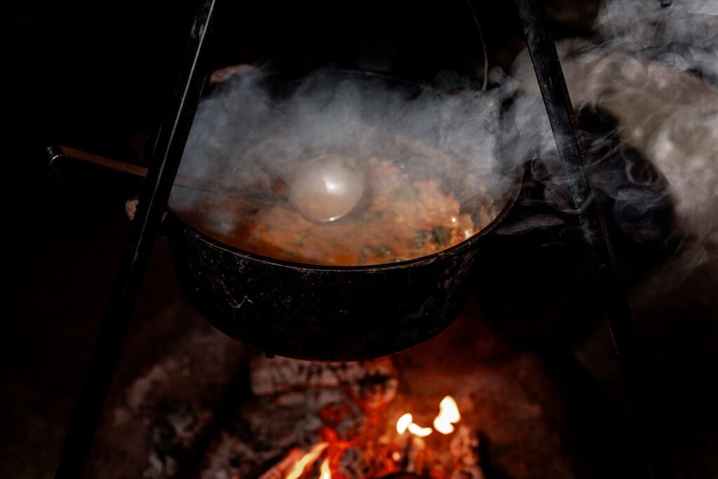Traditionelles Kochen über offenem Feuer mit dampfendem Topf.