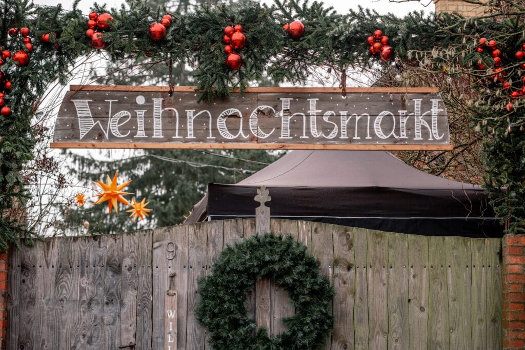 Weihnachtsmarkt mit Tannengirlande und Holzschild in Berlin.
