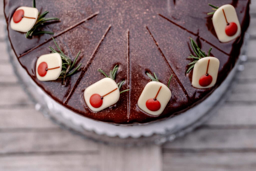 Schokoladenkuchen mit weißen Marzipankirschen und Rosmarin dekoriert.