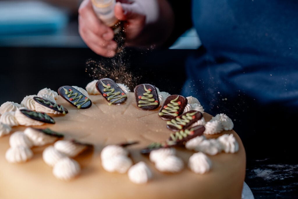 Person dekoriert eine Geburtstagstorte mit Schokoladen-Erdbeeren und Zuckerguss.