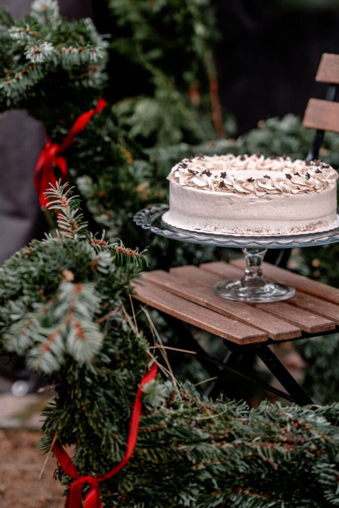 Festliche Torte auf Holztablett vor Weihnachtsbaum mit roten Schleifen.