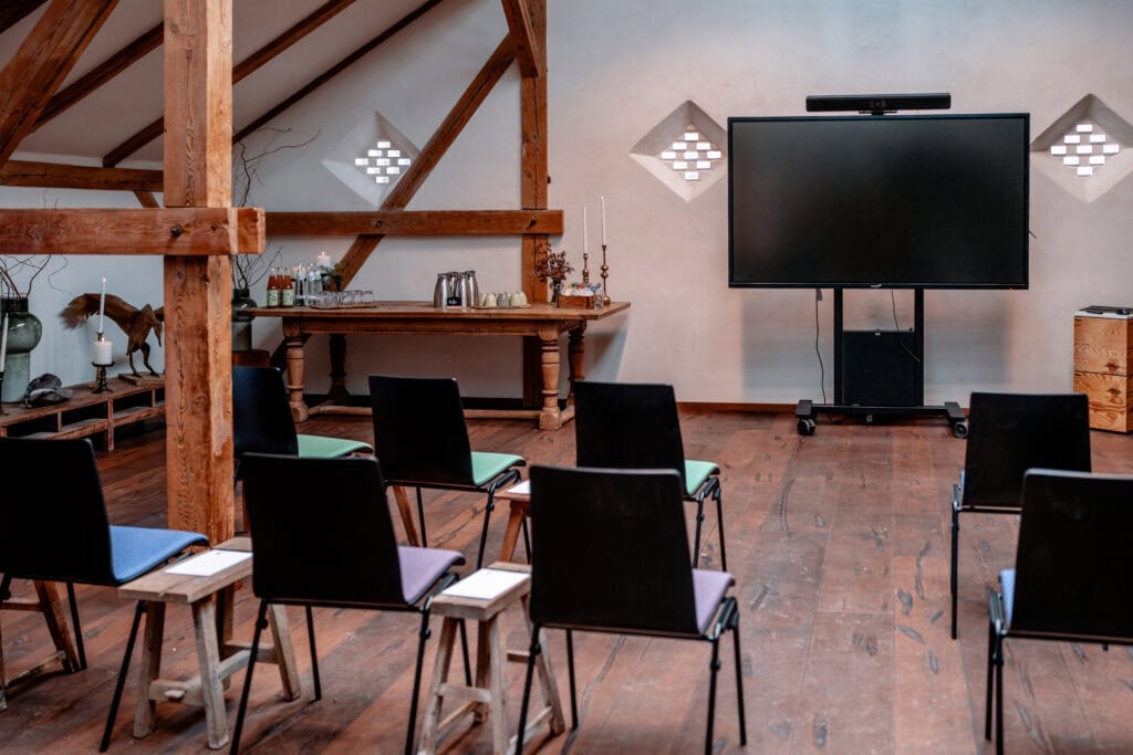 Seminarraum mit Stühlen, Fernseher und Holzdecke bei Gut Leben Berlin.