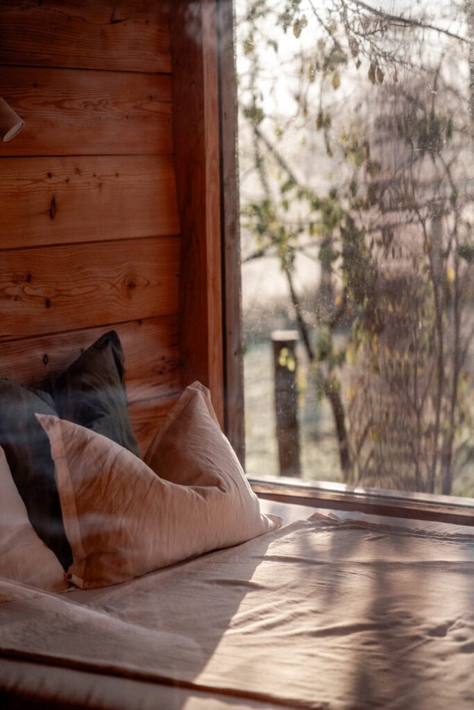 Gemütliches Schlafzimmer mit Holzverkleidung und Sonnenlicht durch das Fenster.