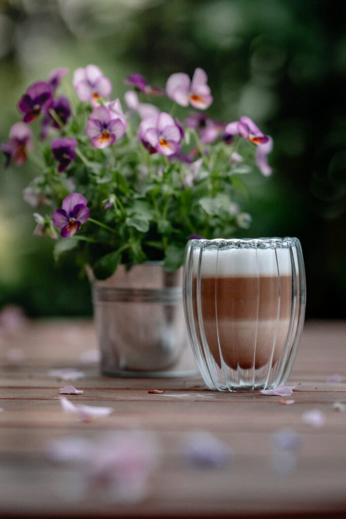 Vase mit bunten Veilchen und einem Glas Kaffee auf Holz Tisch.