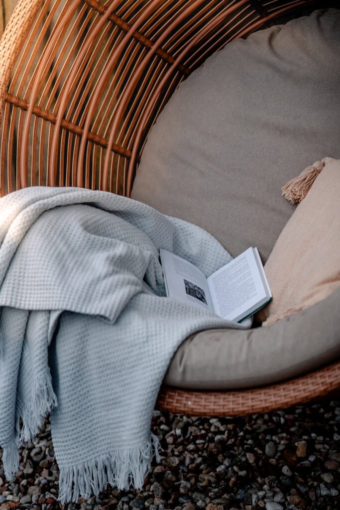 Gemütlicher Leseplatz mit Buch, Decke und Korb-Sessel im Garten.