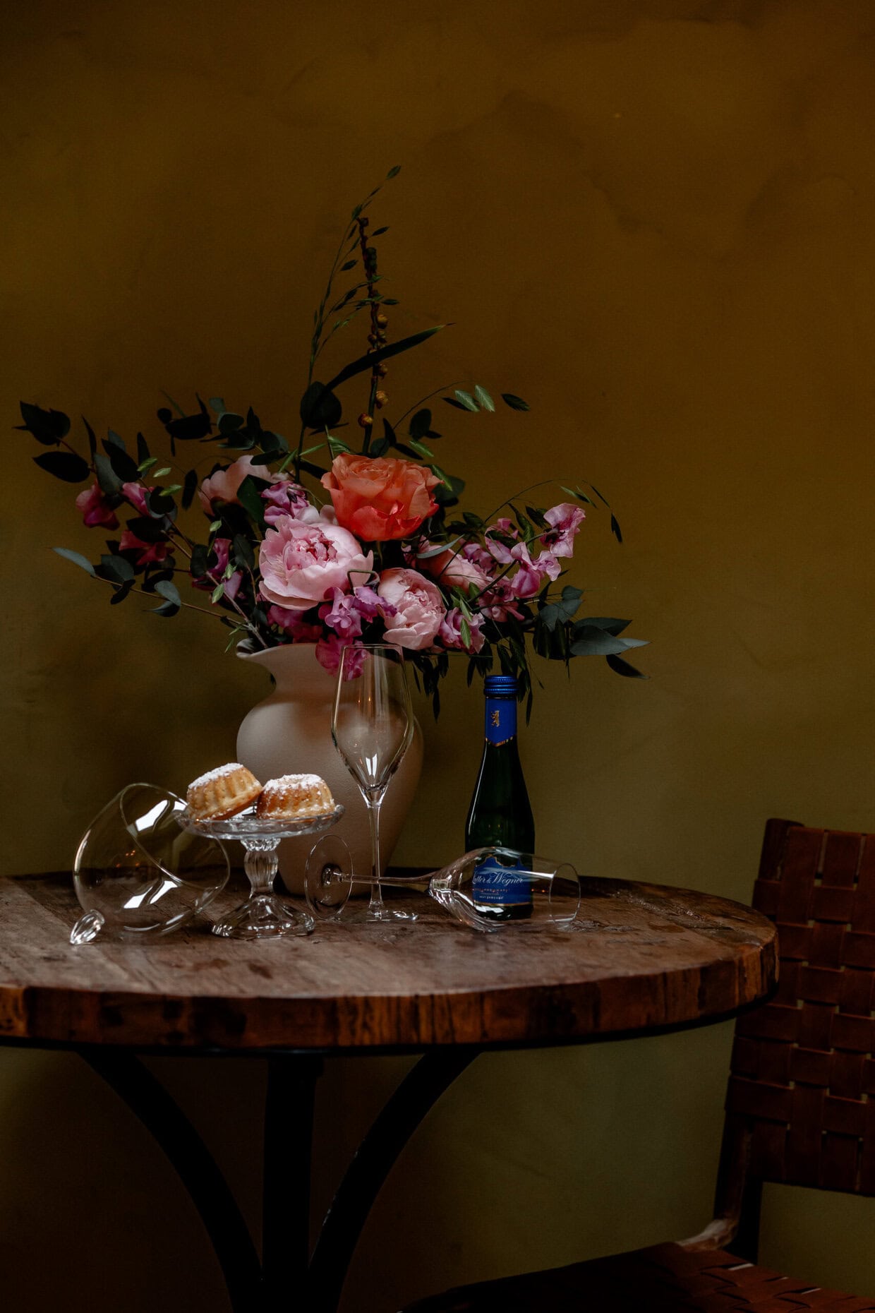 Elegantes Blumenarrangement mit Sekt, Gläsern und Süßigkeiten auf Holztablett.