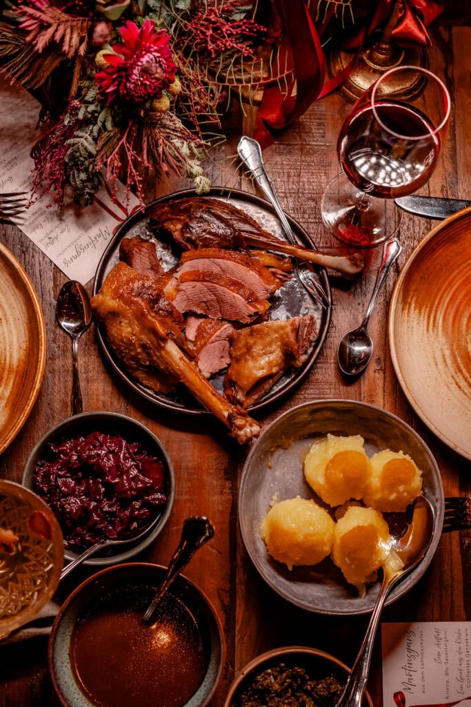 Festliches Weihnachtsessen mit Braten, Beilagen und Rotwein auf Holztafel.