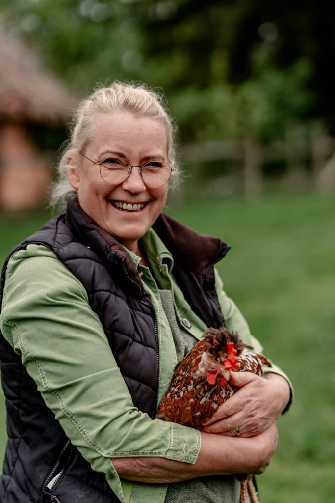 Lächelnde Frau hält Huhn in ländlicher Umgebung bei Gut Leben Berlin.