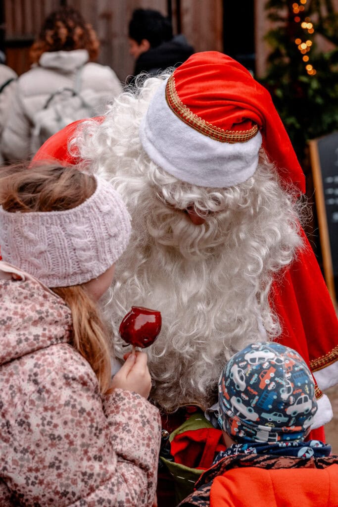 Weihnachtsmann mit Kindern beim Weihnachtsmarkt, festliche Stimmung, Geschenke, Weihnachtszeit.